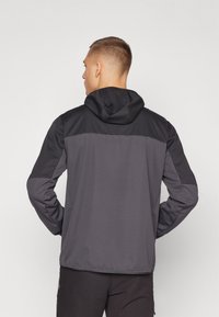 Jachetă pentru bărbați cu glugă, de culoare gri închis, cu un panou superior contrastant negru. Textură netedă, design ajustat și mâneci lungi.