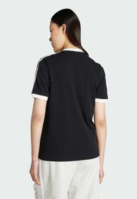 Black cotton t-shirt with white collar and cuff accents. Features a simple design and relaxed fit, showing a smooth fabric texture.