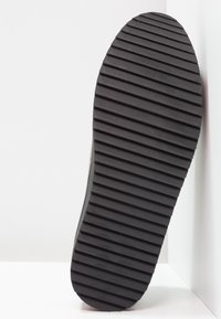 Semelle de chaussure en caoutchouc noir avec de profondes rainures horizontales pour l'adhérence. Bout arrondi et bords lisses. Texture géométrique, design minimaliste.