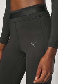 Mustat urheilulegginsit, joissa on sileä ja joustava pinta, leveä vyötärö ja pieni heijastava Puma-logo reidessä.