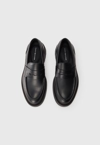 Schwarze Leder Slipper haben eine abgerundete Zehenpartie, sichtbare Nähte und einen glatten Riemen an der Vorderseite. Die Gummisohle sorgt für Grip und Robustheit.