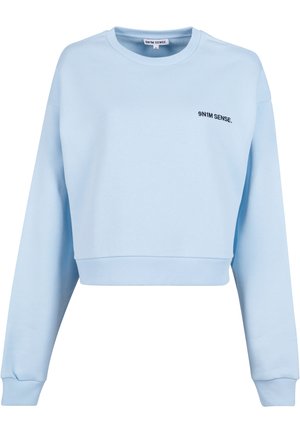 Világoskék, rövidített fazonú pulóver hosszú ujjal, bordázott mandzsettákkal és fekete hímzett „9N1M SENSE.” logóval a mellrészen. Simaszerű textúra.
