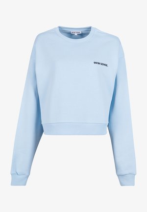 Világoskék, rövidített fazonú pulóver hosszú ujjal, bordázott mandzsettákkal és fekete hímzett „9N1M SENSE.” logóval a mellrészen. Simaszerű textúra.