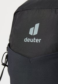 Schwarzer Rucksack aus strukturiertem Nylonmaterial. Verfügt über ein auffälliges, hellblaues "deuter"-Logo und einen Kordelverschluss auf einer Seite.