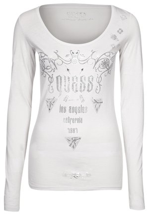 Chemise blanche à manches longues avec col en U, motifs argentés en spirales décoratives, formes géométriques et texte "GUESS, Los Angeles, Californie, 1981."