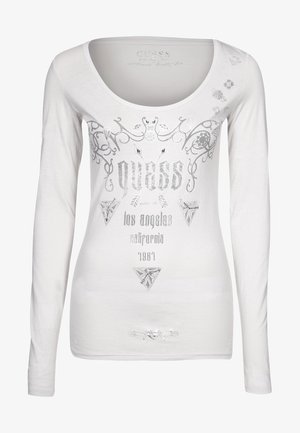 Wit shirt met lange mouwen en een ronde hals, voorzien van zilverkleurige decoratieve spiralen, geometrische vormen en de tekst "GUESS, Los Angeles, Californië, 1981."