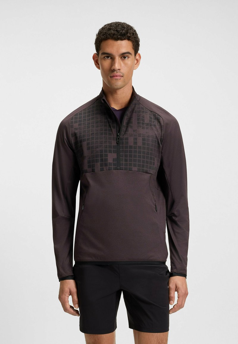 Mörklila idrottströja med halvmage, med ett texturerat geometriskt mönster på den övre framsidan och sidofickor.