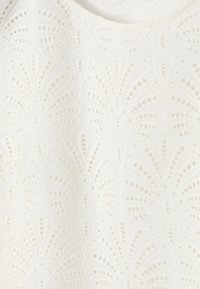 Tissu blanc avec broderie œillet symétrique formant des motifs floraux et en éventail créant un design texturé et aérien.