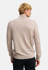 Beige stickad tröja med hög krage och långa ärmar. Den har en mjuk textur och en figurnära design, som passar för lagerpåläggning eller att bäras ensam.