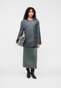 Γκρι σακάκι με ραφινάτο, δομημένο σχέδιο, σε συνδυασμό με μακριά πράσινη φούστα. Αξεσουάρ περιλαμβάνουν τσάντα με μοτίβο ερπετού και μαύρες μπότες.