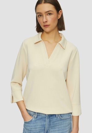 Licht crèmekleurige pullover met een kraag, 3/4 mouwen en een V-hals. Zachte, gladde stof; met zijsplitten aan de zoom voor extra detail.