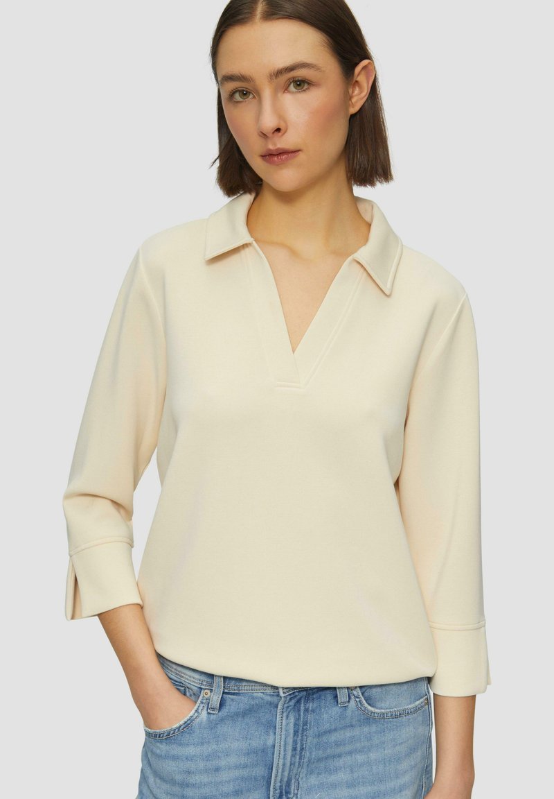 Jasnokremowy sweter z kołnierzykiem, rękawami 3/4 i dekoltem w szpic. Miękka, gładka tkanina; ma boczne rozcięcia na hemie dla dodatkowego akcentu.