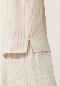 Tenue en lin beige avec de fines rayures verticales et des fentes latérales à la fois sur le haut et le pantalon à jambes larges.
