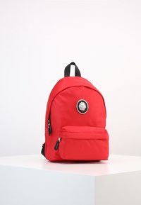 Röd nylonryggsäck med rundad form, svarta detaljer, en ficka med dragkedja fram och en cirkulär logotypdetalj framtill. Justerbara axelremmar ingår.