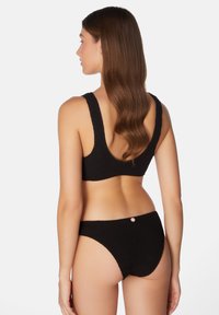 Svart texturerad bikiniuppsättning med en topp med rundad rygg och breda axelband samt låg midjeunderdelar med en liten metallaccent på baksidan.