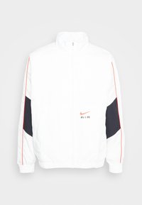 Bílá bunda Nike s vysokým límcem, zipovým uzávěrem, černými akcenty a červenými bočními pruhy. Na hrudi je vyšívané logo. Lehký materiál.