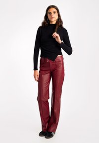 Top de manga larga negro y pantalones de cuero burdeos acampanados con bolsillos frontales y detalles de botones. La modelo lleva zapatillas deportivas negras.