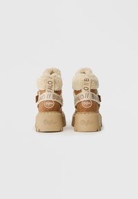 Botas de plataforma marrones con forro de borreguillo beige y correas de marca Buffalo, vistas desde atrás sobre un fondo blanco.