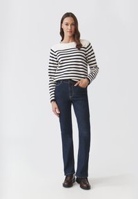 Sweter w paski w kolorze kremowym i granatowym, zestawiony z ciemnoniebieskimi dżinsami. Sweter ma okrągły dekolt i luźny krój; dżinsy mają klasyczny fason.