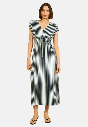 Mujer que lleva un vestido midi sin mangas de rayas verticales negras y blancas, con escote en V y cinturón anudado en la cintura, combinado con sandalias negras.