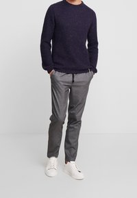 Mörklila stickad tröja med rund halsringning, kombinerad med grå tapered byxor och vita sneakers. Avslappnat outfit med texturerad stickning.