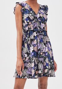 Robe florale avec des manches courtes à volants, décolleté en V, taille cintrée et fond noir. Présente des motifs de feuilles et fleurs tropicales multicolores.