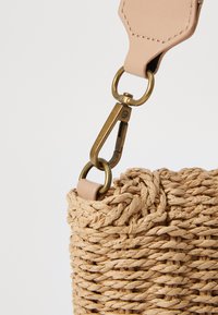 Woven straw handbag in natural color with a textured finish. Features a leather strap and a brass clasp for secure closure.
