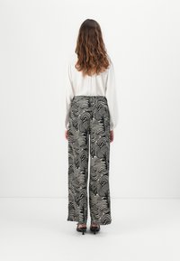 Wide-leg pants in black and cream wavy pattern, featuring an elastic waistband. Paired with a white long-sleeve blouse and black heels.