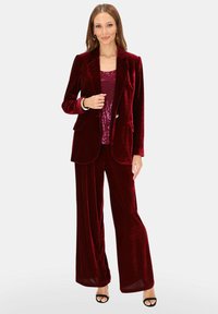 Bordowy aksamitny garnitur trzyczęściowy, składający się z marynarki, błyszczącego topu i szerokich spodni. Gładka faktura z dopasowanym krojem. Marynarka z pojedynczym guzikiem.
