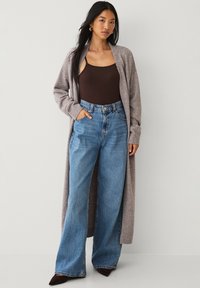 Long grey cardigan made of soft fabric, paired with a brown tank top and high-waisted blue wide-leg jeans. Features a relaxed fit.
