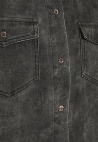 Mörkgrå denimskjorta med två bröstfickor, silverfärgade knappar och ett texturerat tyg med en subtil mönstring.