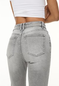 Harmaat korkeavyötäröiset farkut haalistuneella pinnalla, joissa on viisi taskua ja etiketti vyötärönauhassa. Pehmeä, tekstuuri denim-kangas.
