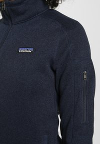 Giacca in pile blu navy con colletto alto. Caratterizzata da una tasca laterale con zip e logo Patagonia sul petto. Tessuto a maglia testurizzato.