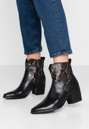 Bottines en cuir noir avec tige texturée effet peau de serpent, talons carrés et fermetures éclair latérales, portées avec un jean bleu court.