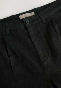Schwarze maßgeschneiderte Hose mit regular Fit, ausgestattet mit einem Knopfverschluss, glatter Stoffstruktur und seitlichen Taschen. Etikett sichtbar.