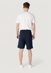 T-shirt blanche et shorts marine en tissu respirant, dotés d'une taille élastique et de poches latérales, portés avec des baskets blanches.