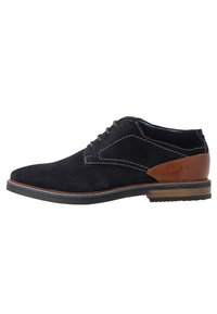Chaussure pour homme avec un dessus en suède noir, un accent en cuir marron au talon, une couture blanche contrastante et un bout arrondi. Semelle en caoutchouc.