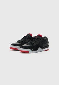 Chaussures de sport noires et grises en matériau daim et mesh, avec des accents rouges, bout arrondi, et semelle en caoutchouc texturée. Design à lacets.