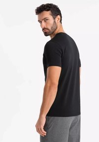 Sort crew neck t-shirt med korte ærmer, glat tekstur, tætsiddende design. Båret med grå bukser, der viser et afslappet look fra ryggen.