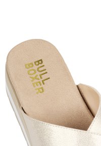 Złote metaliczne sandały na płaskiej podeszwie z teksturowaną, miękką wkładką oraz nazwą marki "BULL BOXER" zapisaną złotymi literami. Posiadają jasną podeszwę.