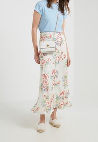 Gonna lunga floreale in tessuto bianco con fiori rossi e blu, abbinata a una maglietta azzurra chiara e a una piccola borsa a tracolla bianca.