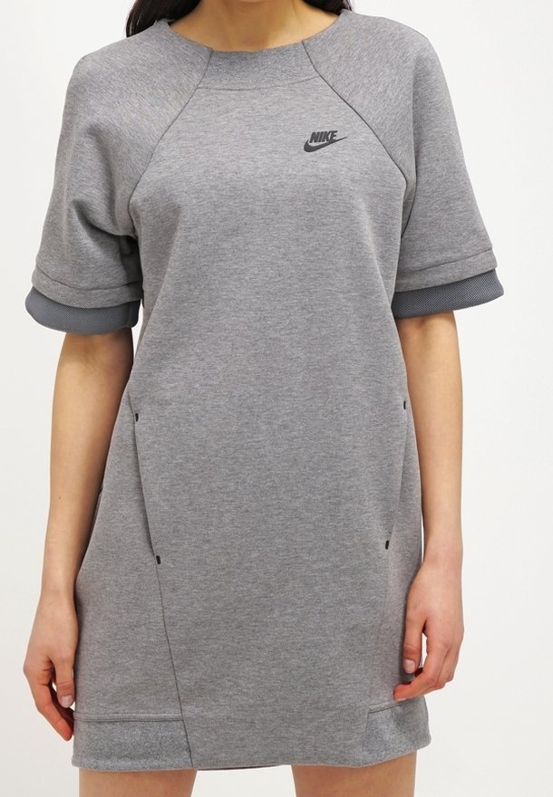 Grå sweatshirtklänning med korta raglanärmar, rundad halsringning, liten svart Nike-logotyp, två sidofickor och texturerade ärmslut.