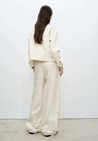 Jachetă din denim de culoare crem și pantaloni evazați. Prezintă o croială lejeră, cusături vizibile, buzunare tip cargo și detalii cu șnur la tiv.