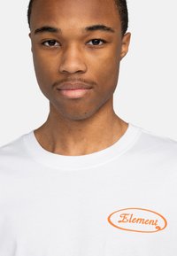 Hvid T-shirt lavet af bomuld, med et orange "Element" logo på venstre bryst. Klassisk crew neck design og blød tekstur.