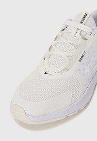 Zapatilla de correr Nike blanca con parte superior de malla, superposiciones texturizadas y sistema de cordones integrado. Cuenta con una suela flexible y detalles de marca sutiles.