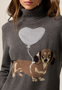 Suéter gris con cuello alto que presenta un diseño de dachshund tejido y un globo plateado en forma de corazón. Material suave con patrones detallados.