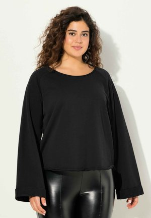 Black long-sleeve top with a rounded neckline and relaxed fit. Soft fabric with a smooth texture and wide sleeves. Paired with shiny black leggings.
