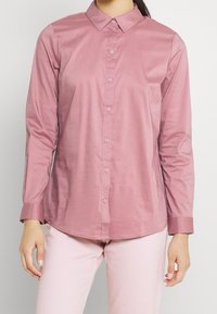 Long-sleeved, pink button-up shirt with a collar, featuring a smooth texture and matching buttons, worn with light pink pants.