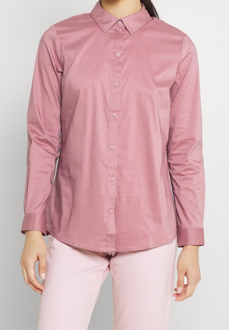 Long-sleeved, pink button-up shirt with a collar, featuring a smooth texture and matching buttons, worn with light pink pants.