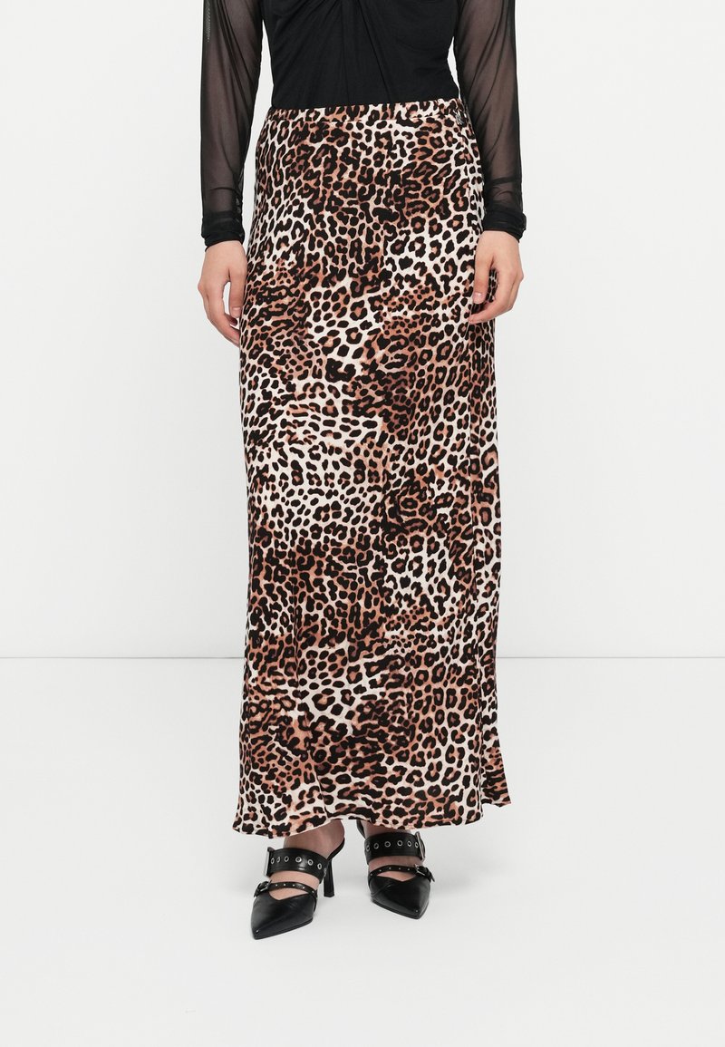 Jupe maxi en imprimé léopard avec une texture douce et fluide dans des tons beiges, marron et noirs ; associée à des escarpins noirs à bout pointu et des accents.